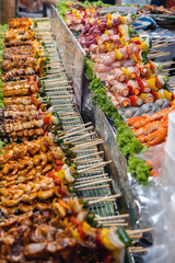 A vibrant night market showcases a colorful assortment of kebabs, including succulent sausages, fresh seafood, prawns, and assorted vegetables on skewers, enticing hungry visitors.