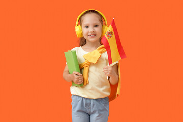 Little girl with Spanish flag and book on orange background