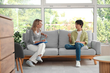 Teenage boy discussing mental health with female psychologist during therapy session on sofa, the psychologist actively listens and takes notes on a clipboard, providing support and guidance © Pixel-Shot