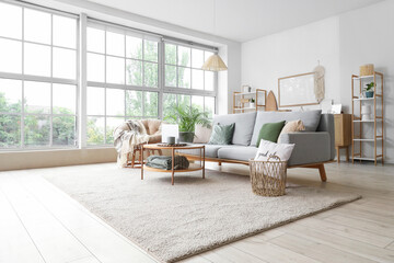 Interior of light living room with grey sofa and modern laptop on coffee table near window