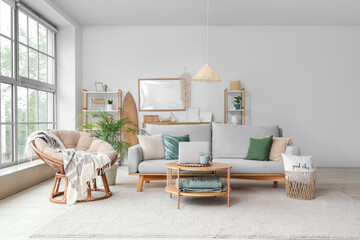 Interior of light living room with grey sofa and modern laptop on coffee table near window