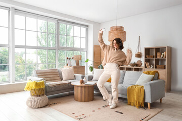 Pretty young woman with mobile phone and headphones dancing in light living room