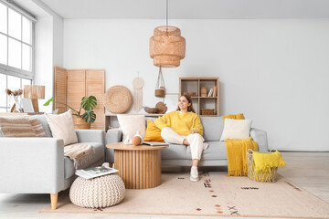 Pretty young woman sitting on grey sofa in light living room