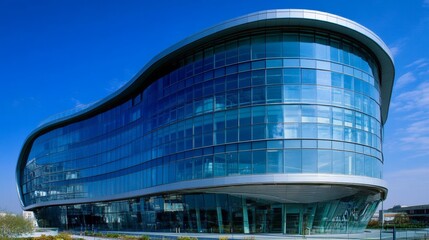 Modern building with curved glass facade reflecting sky. Contemporary architectural design against a clear blue backdrop