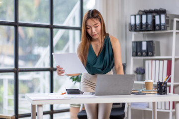 Business Documents,Corporate communication. Happy asian female manager working remotely, reading financial document on Laptop, sitting at desk in the office.