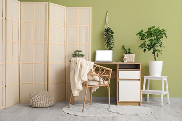 Workplace, houseplant, armchair and folding screen in interior of stylish living room
