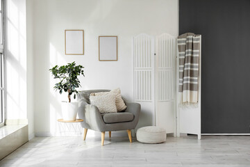 Grey armchair, houseplant, pouf and white folding screen in interior of light living room