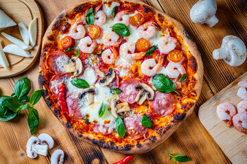 Pizza with two types of toppings, one half paperoni with mushrooms, the other tomatoes and shrimps with cheese. Pizza on a wooden table with ingredients. High quality photo