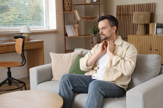 Handsome man self-examining thyroid gland on sofa at home