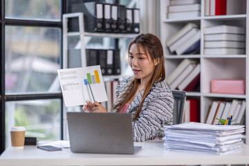 Portrait successful businesswoman, asian woman shows a report of financial documents online interlocutors in the laptop screen, an employee inside an office building online video conference.
