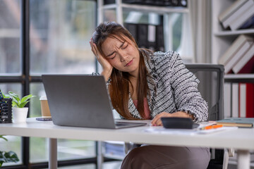 Stressed office worker sitting at desk with laptop feeling burnout. asian woman looking frustrated while working on laptop. Concept of stress, frustration, and burnout in workplace.
