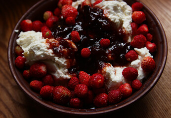 Delicious red fresh strawberries with cottage cheese in a clay plate on a wooden table.