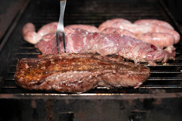 Asado barbecue over grill, cooked and raw close up, fork