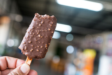 Bitten chocolate popsicle ice cream bar with crushed peanut nuts in hand