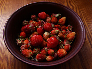 Delicious red fresh strawberries in a clay plate on a wooden table.
