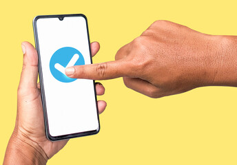 Finger touching check icon on white screen smartphone on yellow background