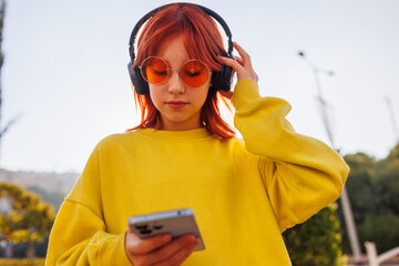 Portrait of a girl with bright hair and facial piercings who uses the phone and listens to music on headphones.