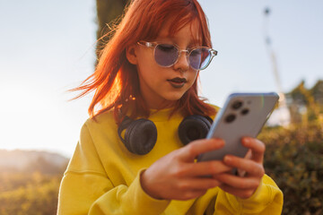 teenage girl with piercings and headphones is typing a message on the phone. stylish teenager chatting with friends.