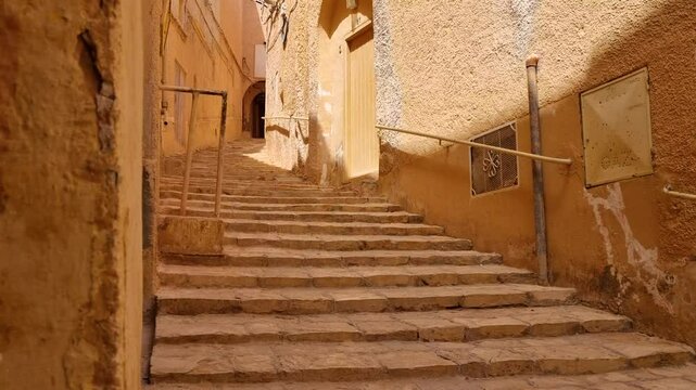 Revealing shot of stair-lined alley and traditional clay houses in old neighborhood of Ghardaia Saharan oasis town in Algeria on sunny day with minaret at the top