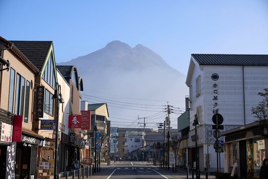 大分、日本 - 2023年11月22日 : 【湯布院】朝霧にかすむ由布岳を背景にした由布院駅前の商店街