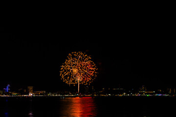Brilliant red fireworks explode against a dark night sky, illuminating a cityscape below. Vibrant...