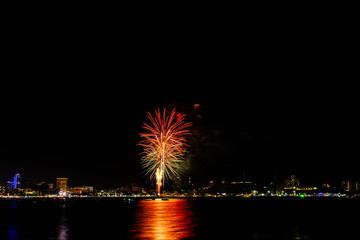 Brilliant red fireworks explode against a dark night sky, illuminating a cityscape below. Vibrant...