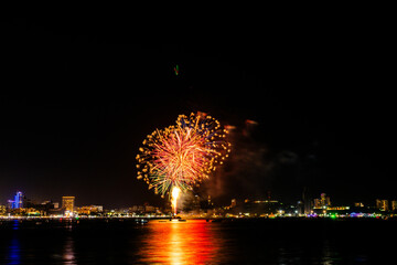 Brilliant red fireworks explode against a dark night sky, illuminating a cityscape below. Vibrant...