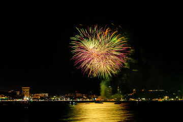 Fototapeta premium Brilliant red fireworks explode against a dark night sky, illuminating a cityscape below. Vibrant bursts and smoke create a festive, dynamic atmosphere, capturing the excitement of celebration.