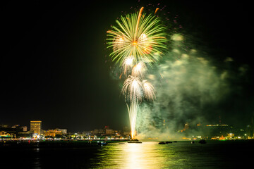 Brilliant red fireworks explode against a dark night sky, illuminating a cityscape below. Vibrant...