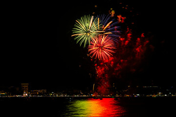 Brilliant red fireworks explode against a dark night sky, illuminating a cityscape below. Vibrant...