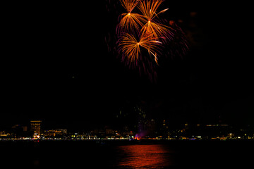 Brilliant red fireworks explode against a dark night sky, illuminating a cityscape below. Vibrant...