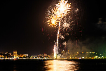 Brilliant red fireworks explode against a dark night sky, illuminating a cityscape below. Vibrant...