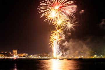 Brilliant red fireworks explode against a dark night sky, illuminating a cityscape below. Vibrant...