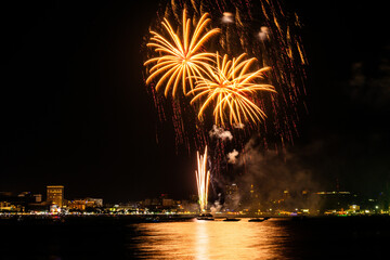 Brilliant red fireworks explode against a dark night sky, illuminating a cityscape below. Vibrant...