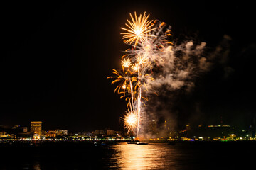 Brilliant red fireworks explode against a dark night sky, illuminating a cityscape below. Vibrant...
