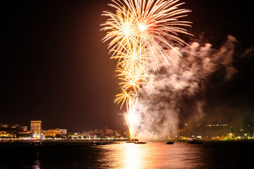 Brilliant red fireworks explode against a dark night sky, illuminating a cityscape below. Vibrant...