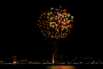 Brilliant red fireworks explode against a dark night sky, illuminating a cityscape below. Vibrant...