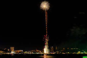Brilliant red fireworks explode against a dark night sky, illuminating a cityscape below. Vibrant...