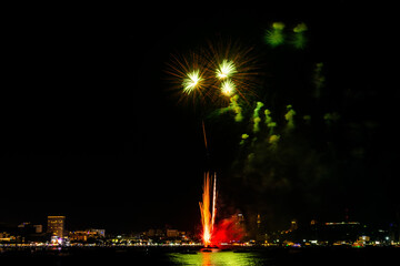 Brilliant red fireworks explode against a dark night sky, illuminating a cityscape below. Vibrant...