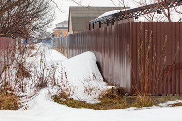 A fence is covered in snow and has a pile of snow on it