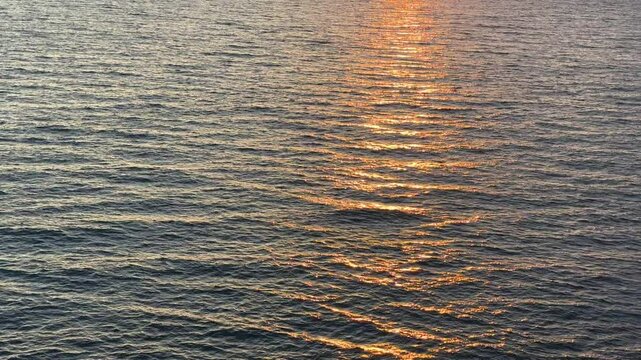 Calm flowing sea water with sunset reflections on surface.