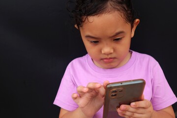 Asian girl child is seriously using cell phone with adorable face, close up view.