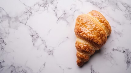 A freshly baked croissant on a white marble surface.