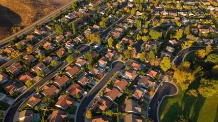 An aerial view of a tranquil suburban neighborhood showcases picturesque homes and towering trees, all aglow in a stunning sunset, epitomizing the American dream of ideal living and community harmony