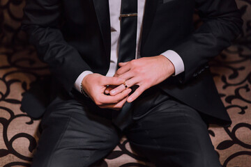 A man in a suit and tie is sitting on a couch. He is holding a ring in his hand