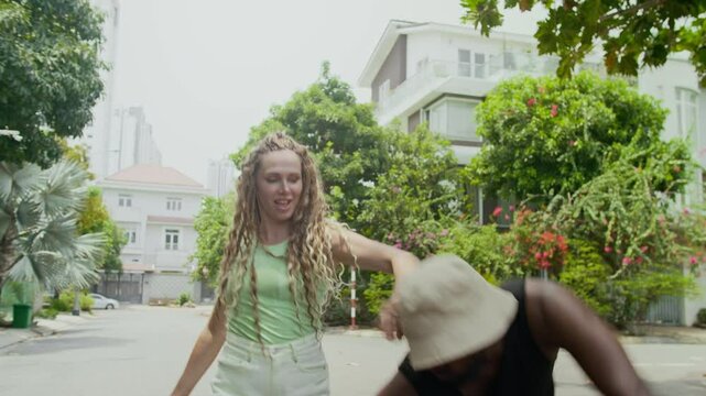 Handheld shot of bicultural young man and woman in activewear performing contemporary dance moves on street