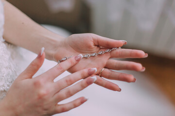 A woman is holding a necklace in her hands. The necklace is silver and has a diamond pendant. The woman is wearing a white dress and has her nails painted. Concept of elegance and sophistication