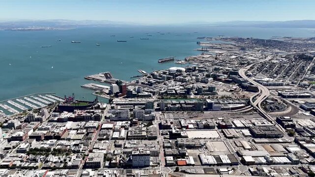 Aerial view over San Francisco Bay and the Mission Bay area, showing Oracle Park, Chase Center, marinas, and the sprawling urban landscape. Ships are anchored in the bay, with the city&acirc;&euro;&trade;s waterfront