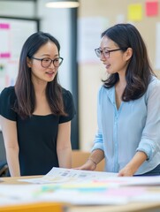 Two Asian women discussing marketing strategy, bright office, teamwork and planning