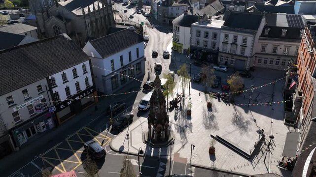 Rossmore Monument, Monaghan Town, County Monaghan, Ireland, April 2023. Drone orbits counter clockwise and pulls backward above the Memorial in the center of the Diamond as light traffic passes by.